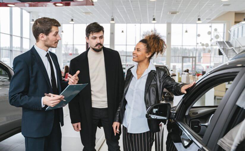 Venditore auto con due clienti in concessionarioche parlano dell'assistenza stradale